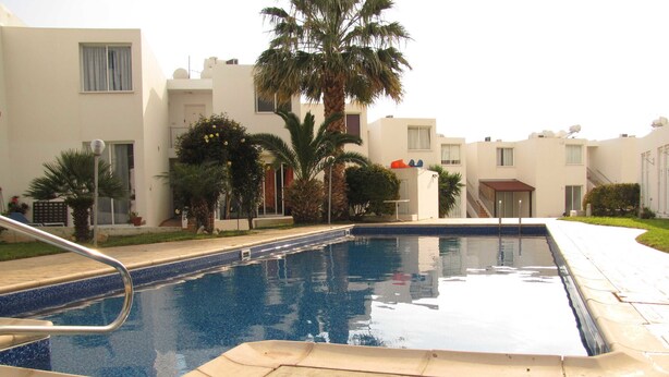 A swimming pool with a tiled deck, surrounded by palm trees and modern buildings. - Webooking Pegia Apartment (Pegeia)