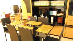 A dining area with a table and chairs, a television, and shelves with books and decorative items. - Webooking Pegia Apartment (Pegeia)