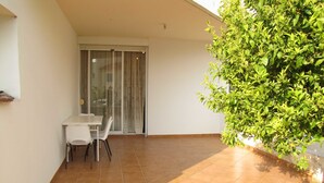 A small patio with a table and chairs, a sliding glass door, and a green plant. - Webooking Pegia Apartment (Pegeia)