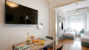 A modern living room with a flat-screen TV mounted on the wall, a dining area with a table set for two, and a cozy seating area with a sofa and a hanging light fixture. - Attractive Flat near the Acropolis Museum - Athenian Homes, Athenian Homes (Athens)