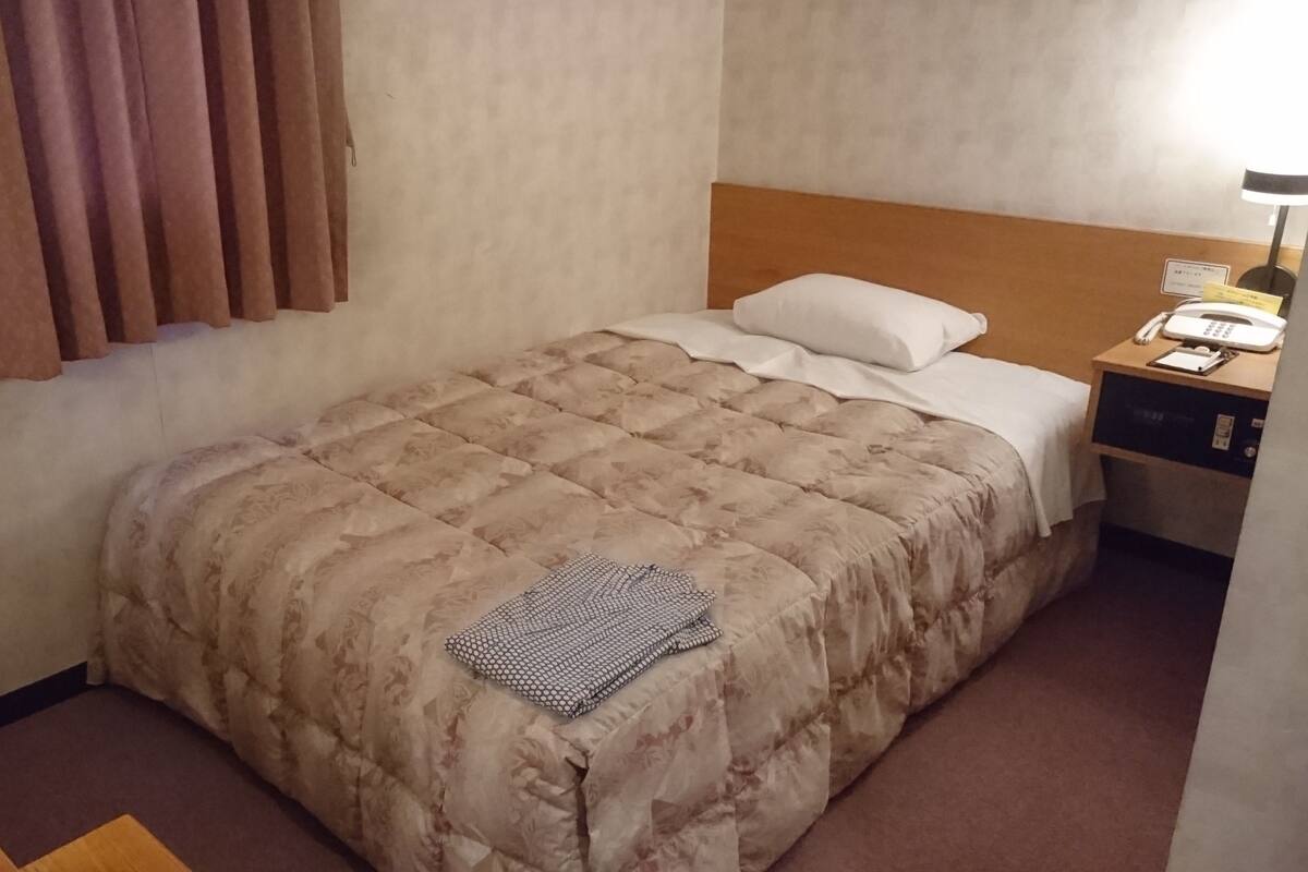 A hotel room with a bed, a nightstand, a lamp, and a chair.