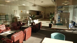 A hotel lobby with leather seating, a reception desk, and a refrigerator stocked with beverages. - Mihara Kokusai Hotel (Mihara)