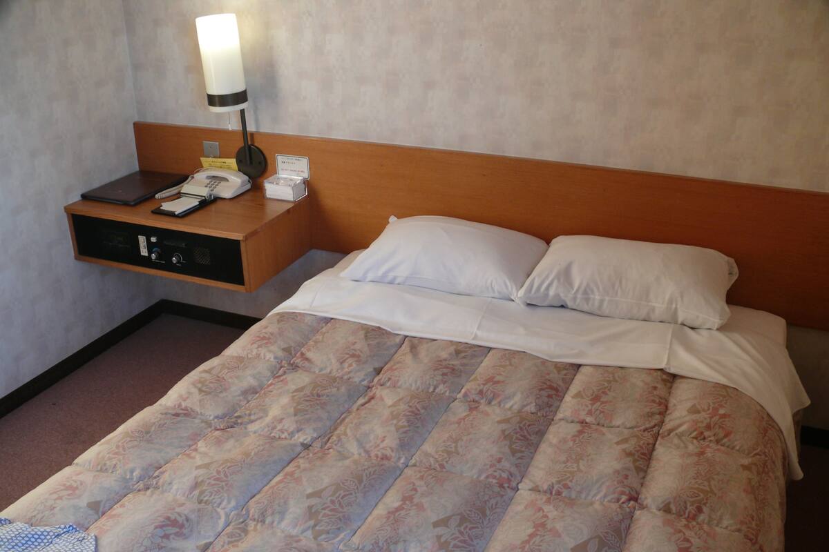 A hotel room with a bed, a nightstand, a lamp, and a telephone.