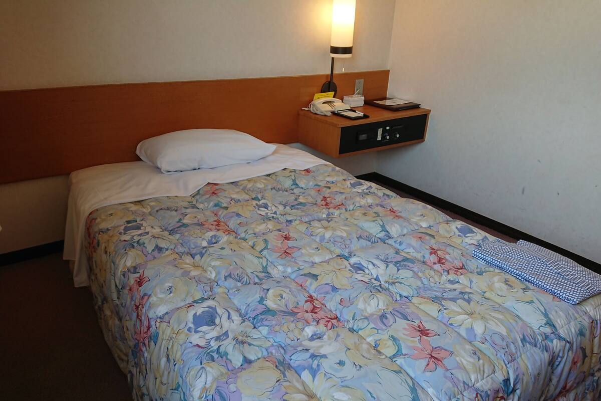 A hotel room with a bed, a nightstand with a lamp, a phone, and a small table.