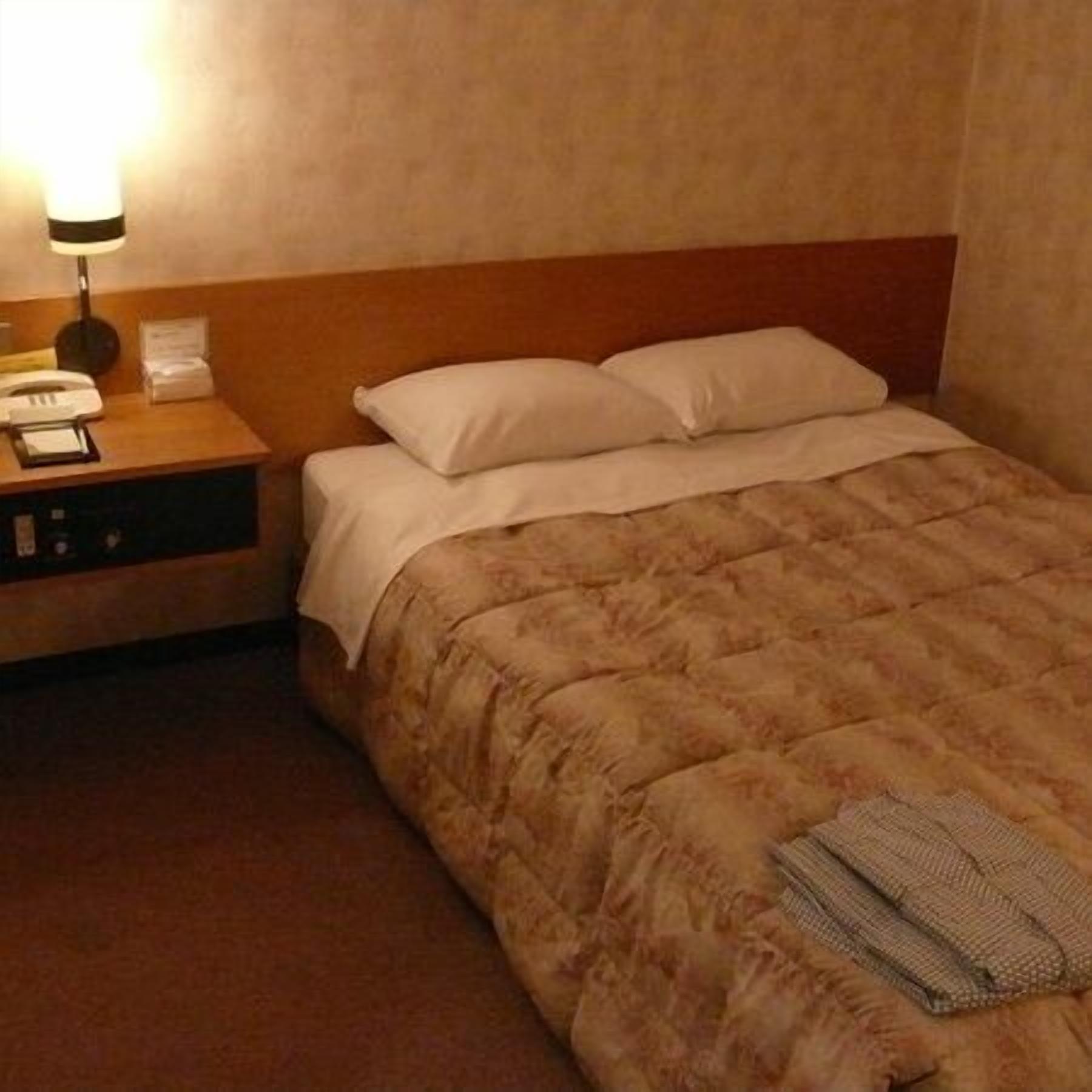 A hotel room with a bed, a nightstand with a lamp, a telephone, and a small table.