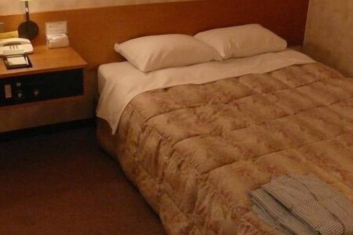 A hotel room with a bed, a nightstand with a lamp, a telephone, and a small table.