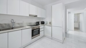 Una cocina moderna con armarios blancos, un lavamanos de acero inoxidable, horno empotrado y microondas.