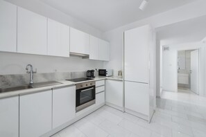 A modern kitchen with white cabinets, a stainless steel sink, a built-in oven, and a microwave.