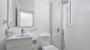 Un baño moderno con ducha de vidrio, inodoro y lavamanos con espejo.