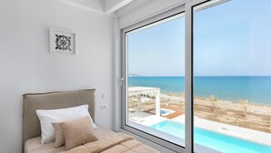Un dormitorio con un ventanal grande, una cama con ropa de cama color beige y un cuadro en la pared.