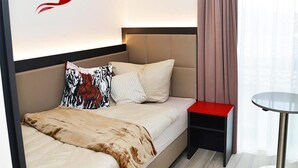 A modern hotel room with a bed, a red table, and a window with curtains. - Hotel Rotes Einhorn (Dueren)