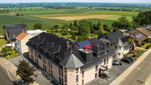 A multi-story building with solar panels on the roof, surrounded by green fields and trees. - Hotel Rotes Einhorn (Dueren)