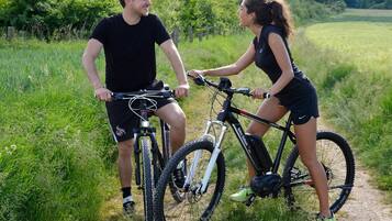 Two people on bicycles on a dirt path surrounded by greenery.