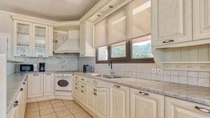 A kitchen with white cabinetry, a built-in oven, a microwave, and a window above the sink. - Ananta Blue Four Bedroom Apartment with full Sea View (Ξηροκάστελλο)