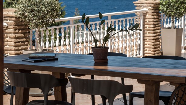 A wooden table with chairs, a potted plant, and a view of the sea. - Ananta Blue Four Bedroom Apartment with full Sea View (Ξηροκάστελλ ο)
