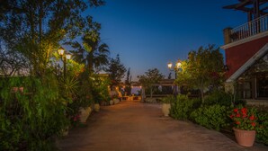 A pathway leading to a building with a red exterior, surrounded by lush greenery and potted plants. - Ananta Blue Four Bedroom Apartment with full Sea View (Ξηροκάστελλο)
