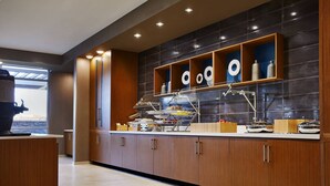 A modern kitchen with wooden cabinets, a countertop with various kitchen items, and a wall-mounted shelf with decorative objects. - SpringHill Suites by Marriott Springfield North (Springfield)