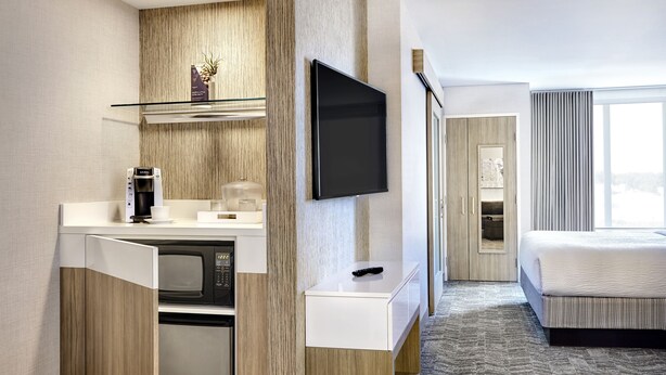 A modern hotel room with a kitchenette, a flat-screen TV, a bed, and a large window. - SpringHill Suites by Marriott Springfield North (Springfield)
