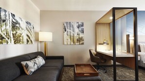 A modern hotel room with a dark grey sofa, a wooden side table, a desk with a chair, and two abstract paintings on the walls. - SpringHill Suites by Marriott Springfield North (Springfield)