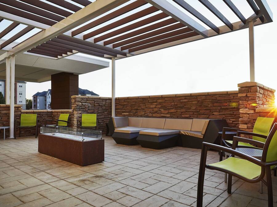 An outdoor patio area with a stone wall, wooden pergola, and seating arrangements including a sofa and chairs.