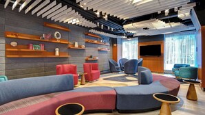 A modern lounge area with a curved seating arrangement, built-in shelves, and a flat-screen TV. - SpringHill Suites by Marriott New York Midtown Manhattan/Park Avenue (New York)