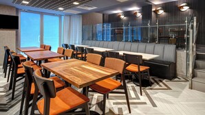 A modern restaurant with wooden tables and orange cushioned chairs, a glass partitioned booth area, and large windows providing natural light. - SpringHill Suites by Marriott New York Midtown Manhattan/Park Avenue (New York)