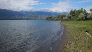 Un lac bordé de montagnes en arrière-plan et d’une zone herbeuse le long de la rive.