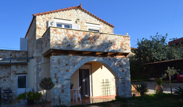 Une maison en pierre à deux étages, avec un toit en tuiles, une entrée en arc de cercle et un petit balcon.