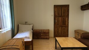 A small, cozy room with a bed, a wooden chest of drawers, a wooden table, and a brown sofa. - Castle-Wall-Inn - Hostel (Mikulov)