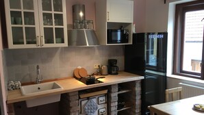 A kitchen with a sink, stove, microwave, and refrigerator. There are cabinets above the counter and a window with a view outside. - Castle-Wall-Inn - Hostel (Mikulov)