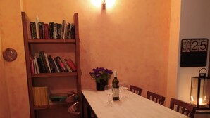 A cozy dining area with a wooden table, chairs, a bookshelf, and a wall-mounted light fixture. - Castle-Wall-Inn - Hostel (Mikulov)