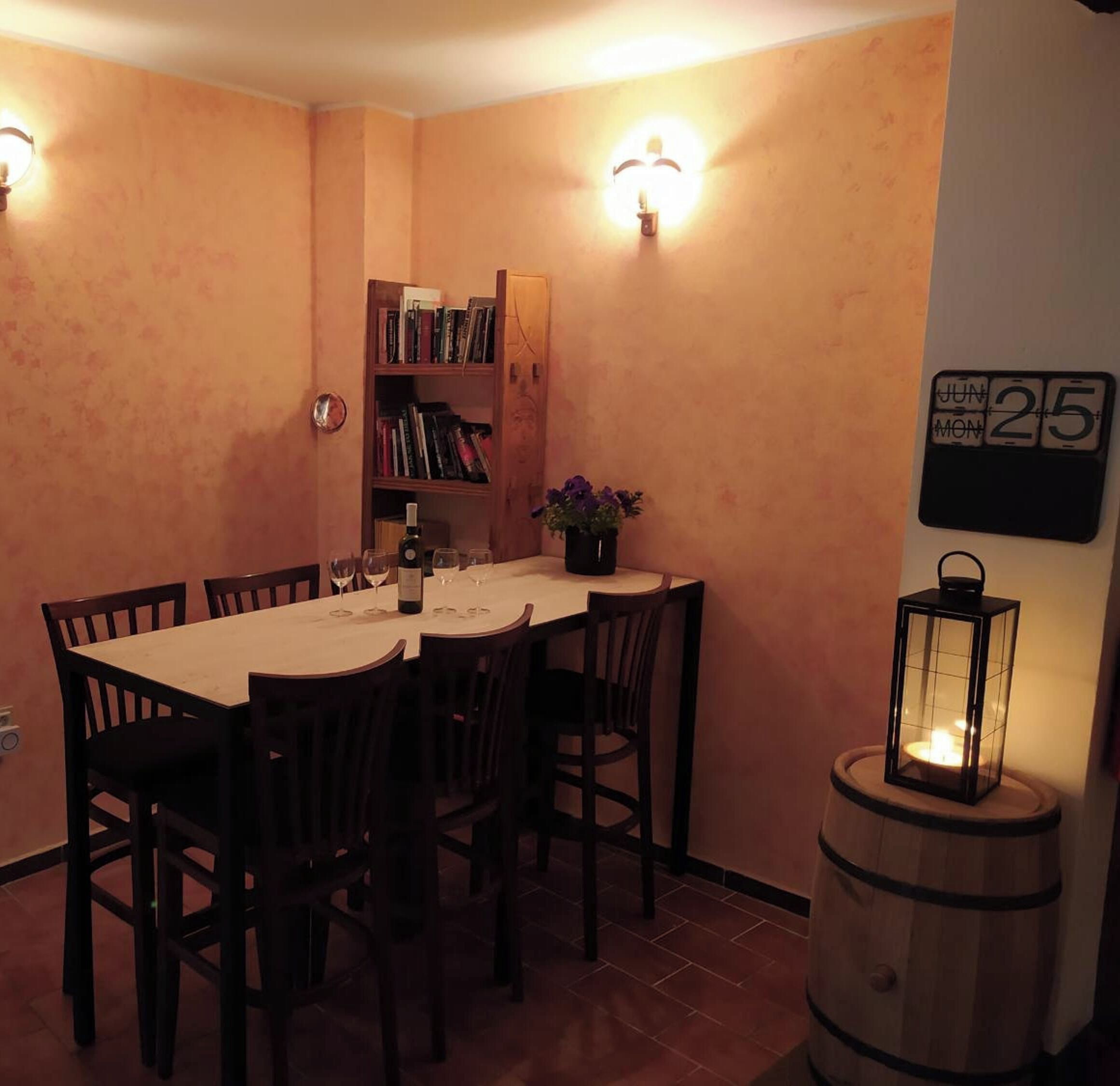 A dining area with a table set for four, surrounded by chairs, a bookshelf, and a wall-mounted calendar.