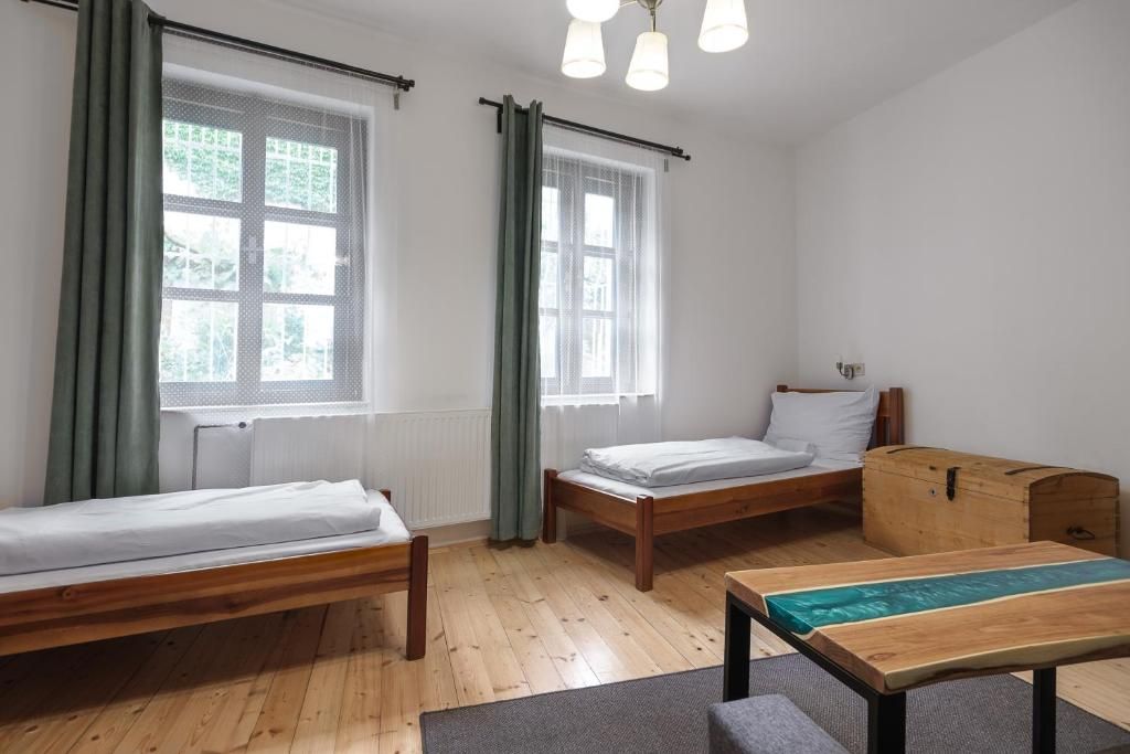 A room with two wooden beds, a wooden table, and a window with curtains.