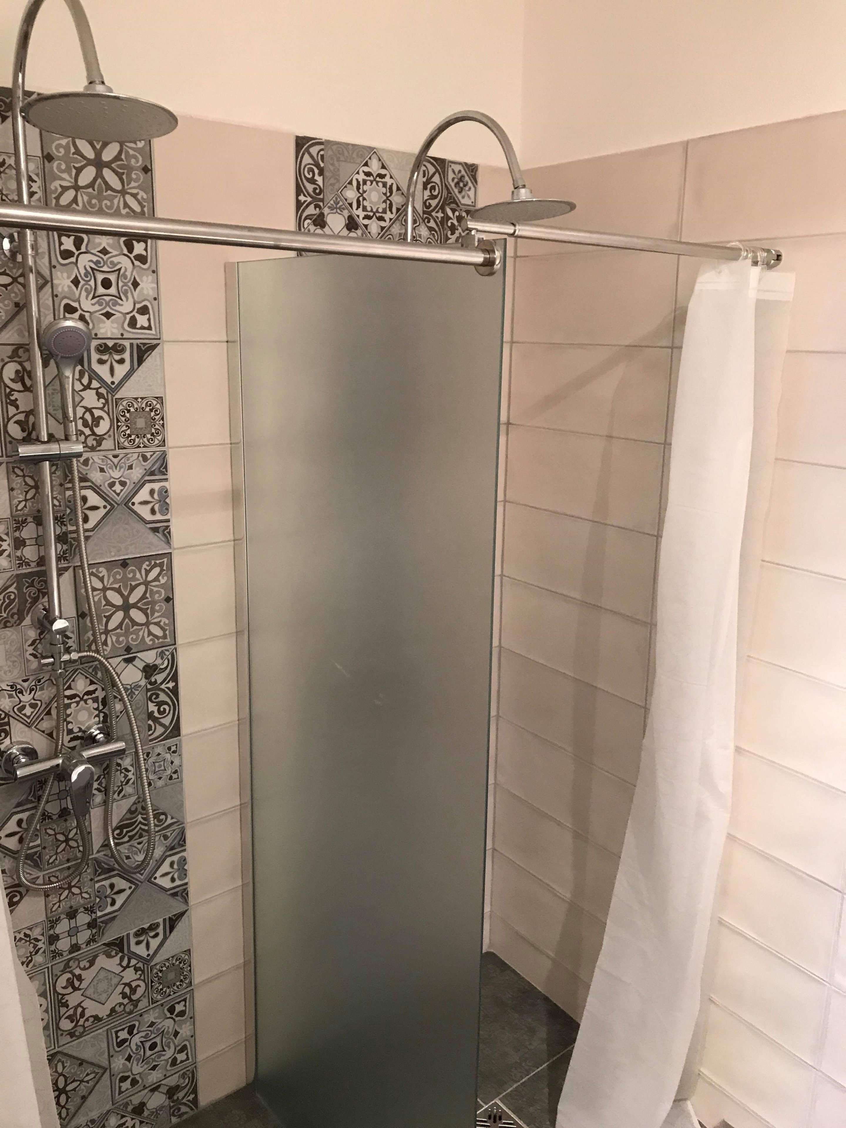A shower with a glass door, a handheld showerhead, and a wall-mounted faucet.