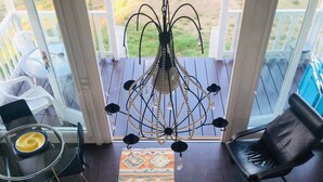 A sunroom with a glass door, a chandelier, a black leather chair, a glass table, and a patterned rug. - Playa di Valverde - Campsite (Galliate)
