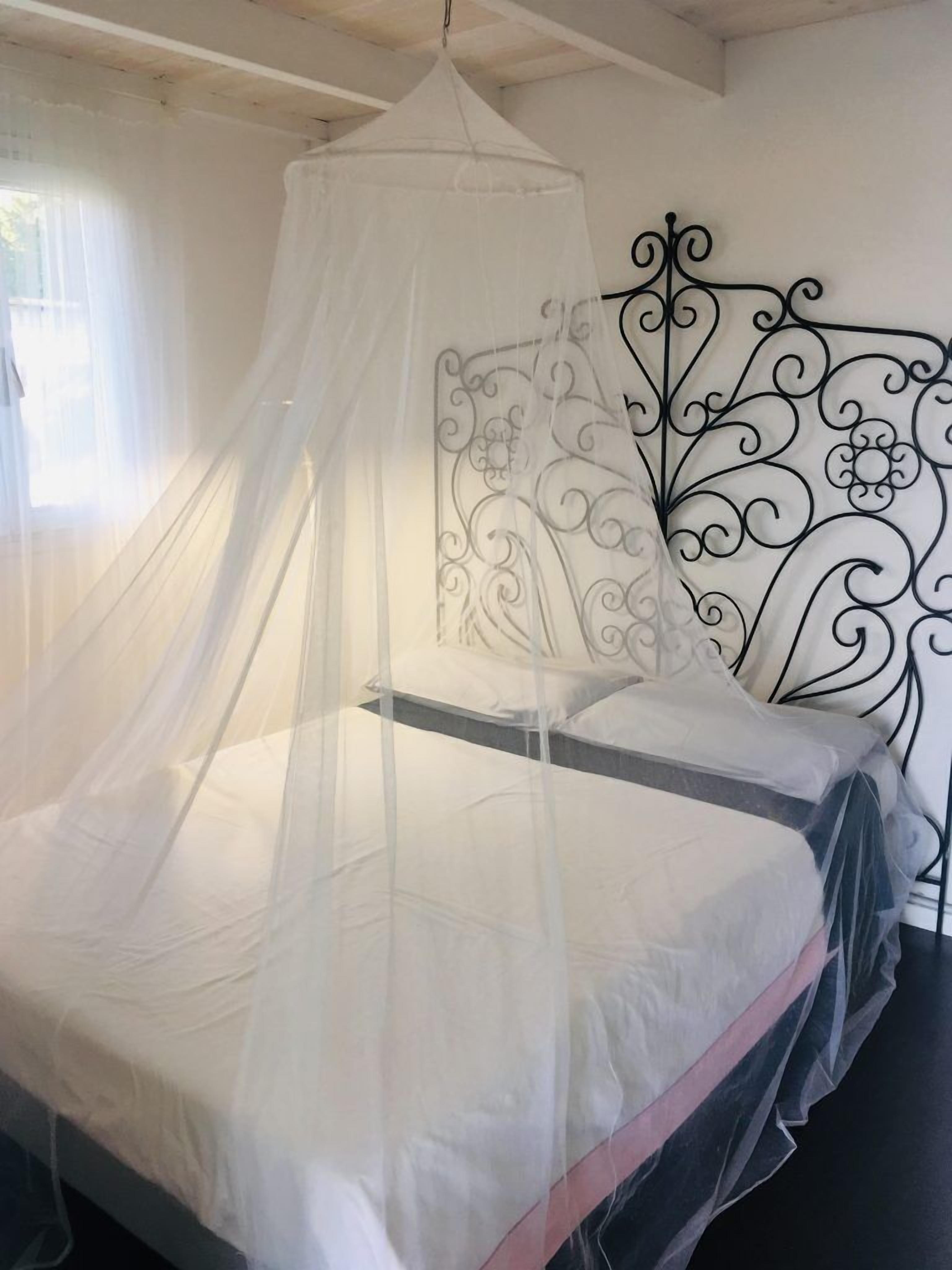 Una cama con dosel, cabecera de metal decorativa y ventana con cortinas.