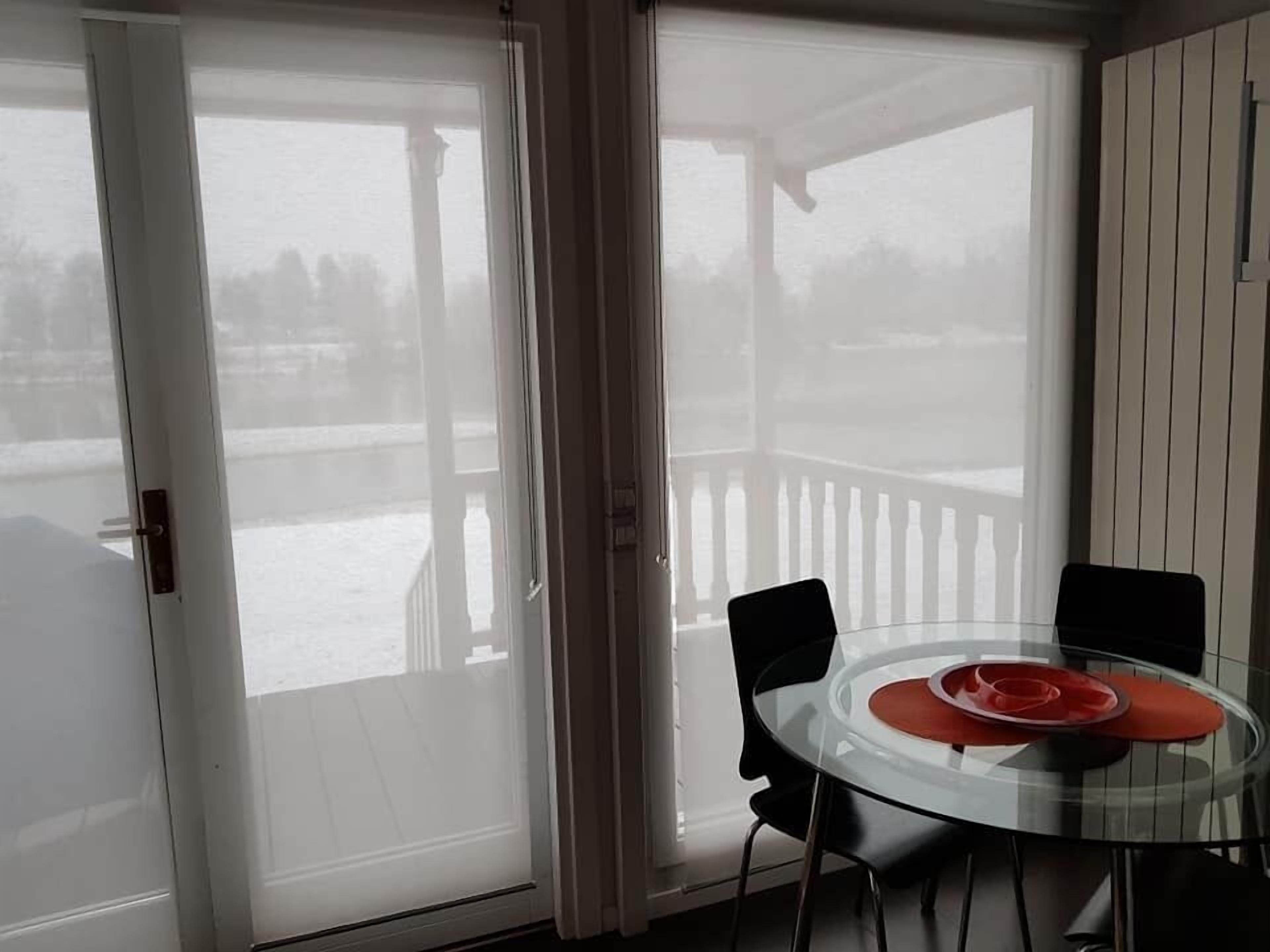 A glass-top table with chairs, a red placemat, and a view of a snowy deck through a sliding glass door.