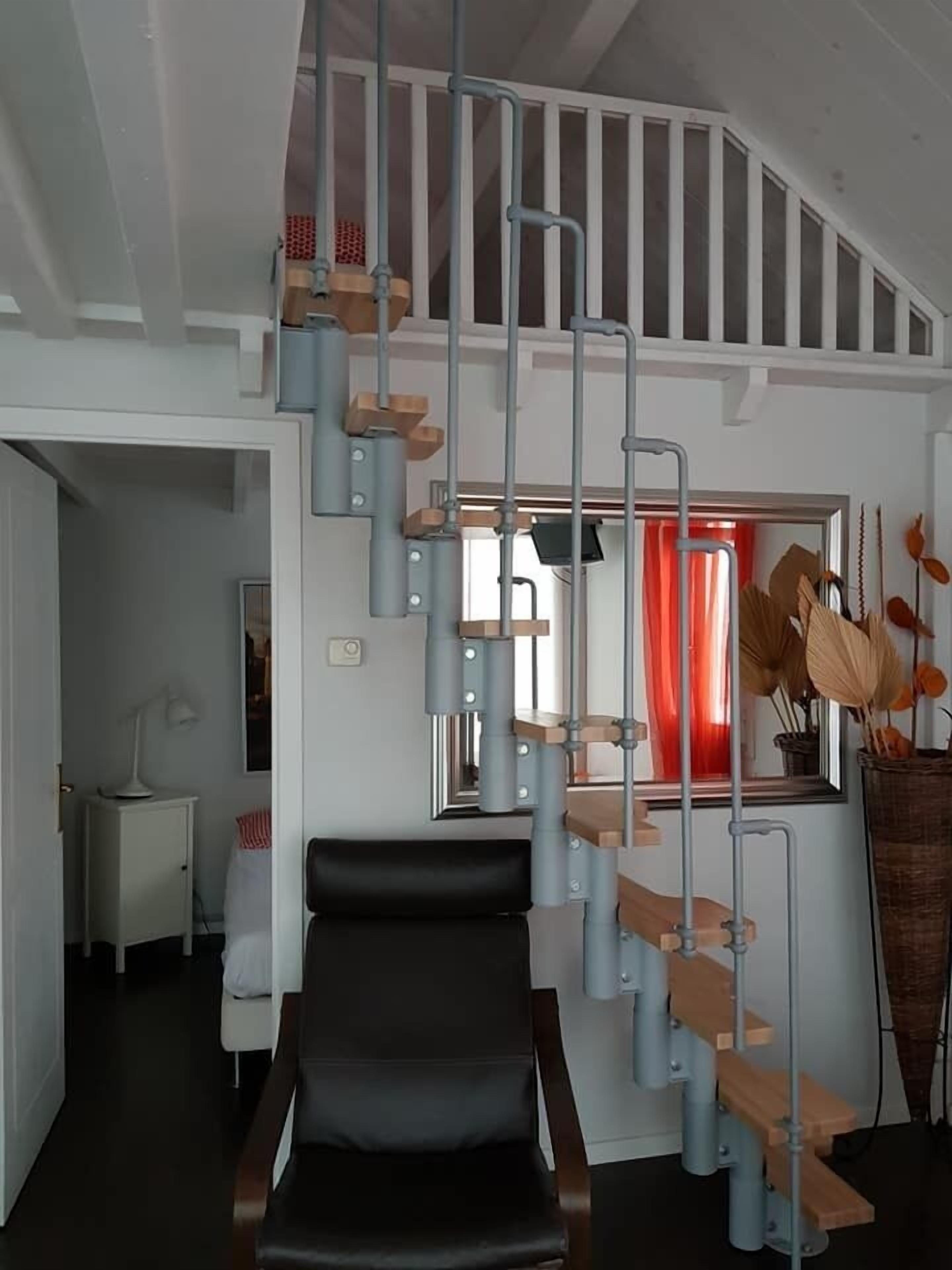 Un intérieur moderne avec un fauteuil noir, un escalier à marches en bois et un rideau rouge en arrière-plan.