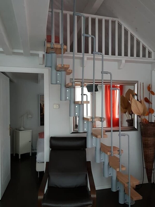 Un interior moderno con una butaca negra, una escalera con escalones de madera y una cortina roja al fondo.