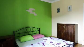 A bedroom with a green wall, a bed with a floral bedspread, a wooden wardrobe, and a small nightstand.
