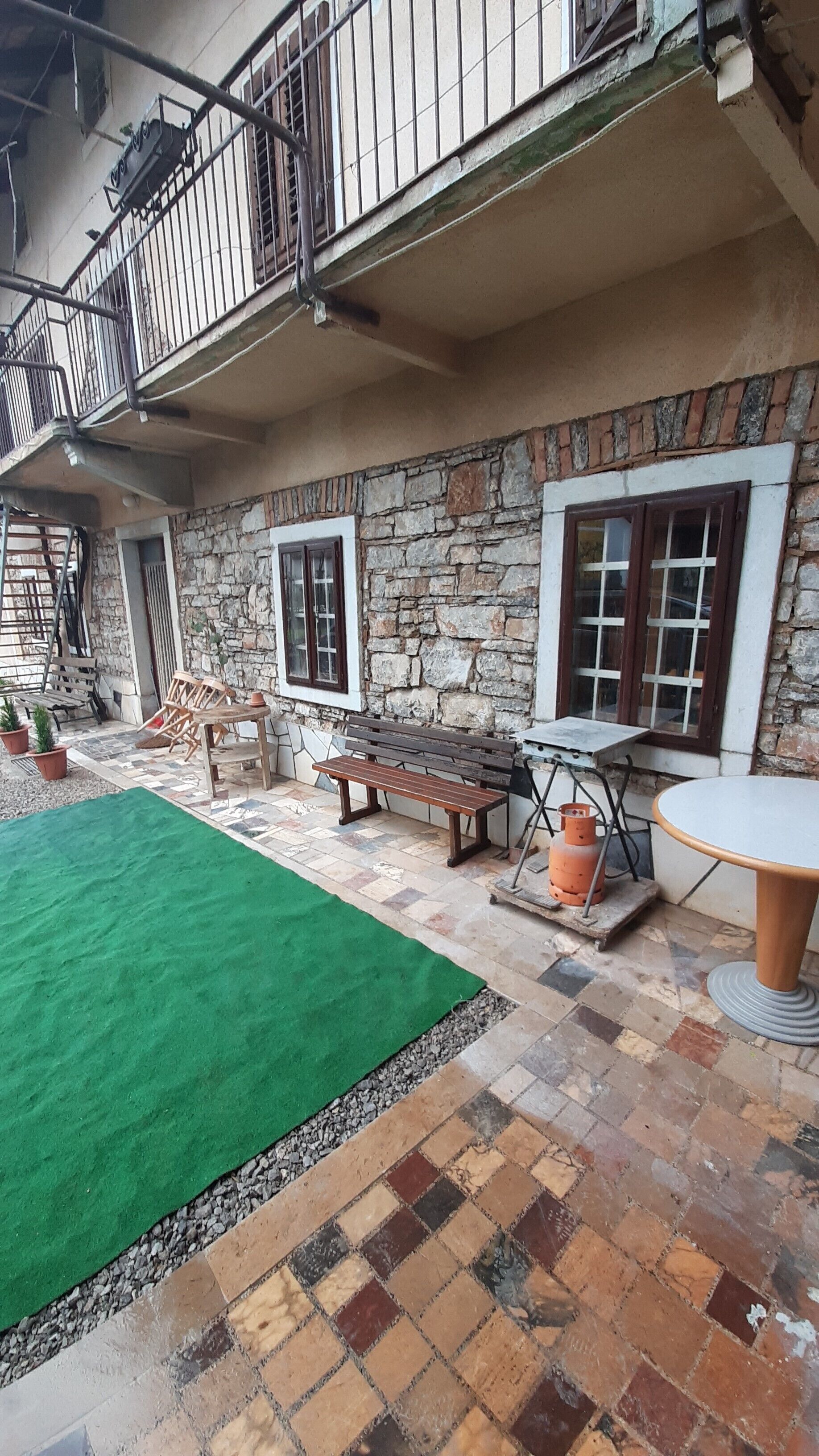 Un cortile con un prato artificiale verde, una panchina di legno, un tavolo e un muro in pietra.