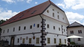 A white building with a red-tiled roof, multiple windows, and a bench area with an umbrella. - Apartments Mozinetova hisa (Dobrova-Polhov Gradec)