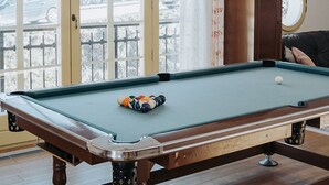 A pool table in a room with large windows, a wooden floor, and a ceiling light. - Apartments Mozinetova hisa (Dobrova-Polhov Gradec)