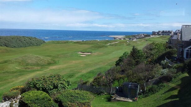 A golf course with a view of the ocean and a residential area with houses. - Homesly The Station Hotel (Banff)