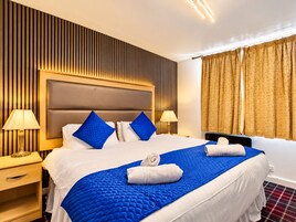 A hotel room with a large bed, two bedside tables, a headboard, and a window with curtains.