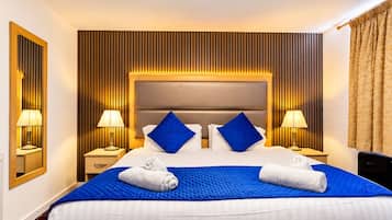 Una habitación de hotel con una cama grande, dos mesitas de noche con lámparas, un cabecero y un espejo en la pared.