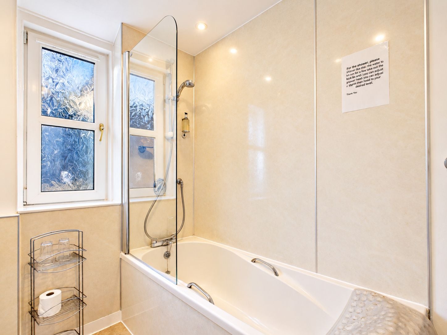 A modern bathroom with a glass-enclosed shower, a bathtub, and a window with frosted glass.