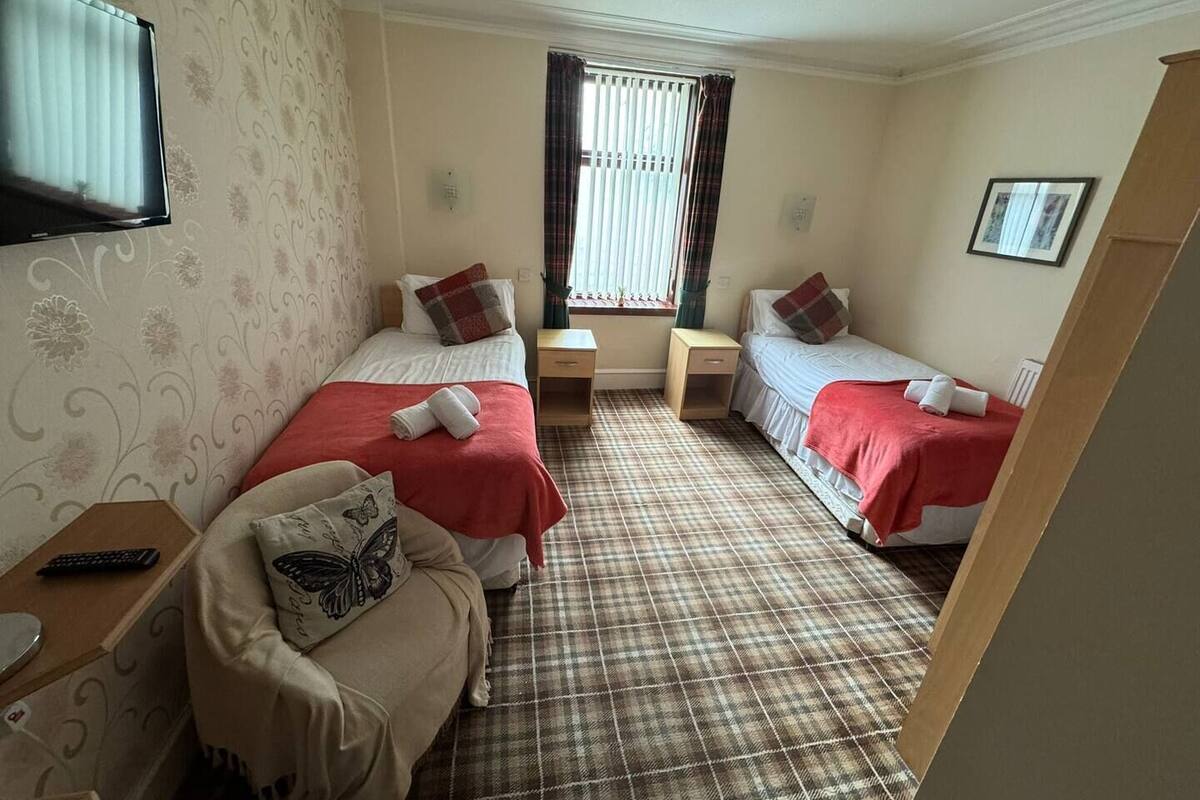 A hotel room with two beds, a TV, a window with curtains, and a plaid carpet.
