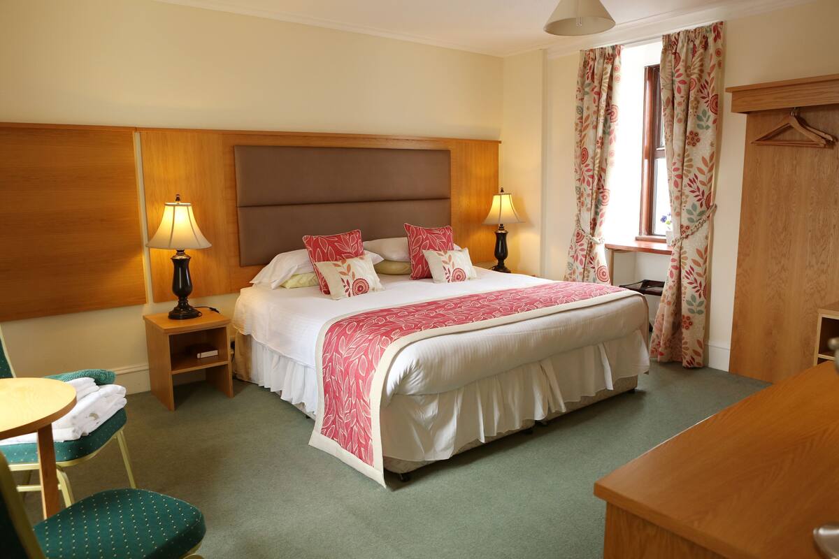 A hotel room with a large bed, two bedside tables with lamps, a chair, a desk, and a wardrobe.