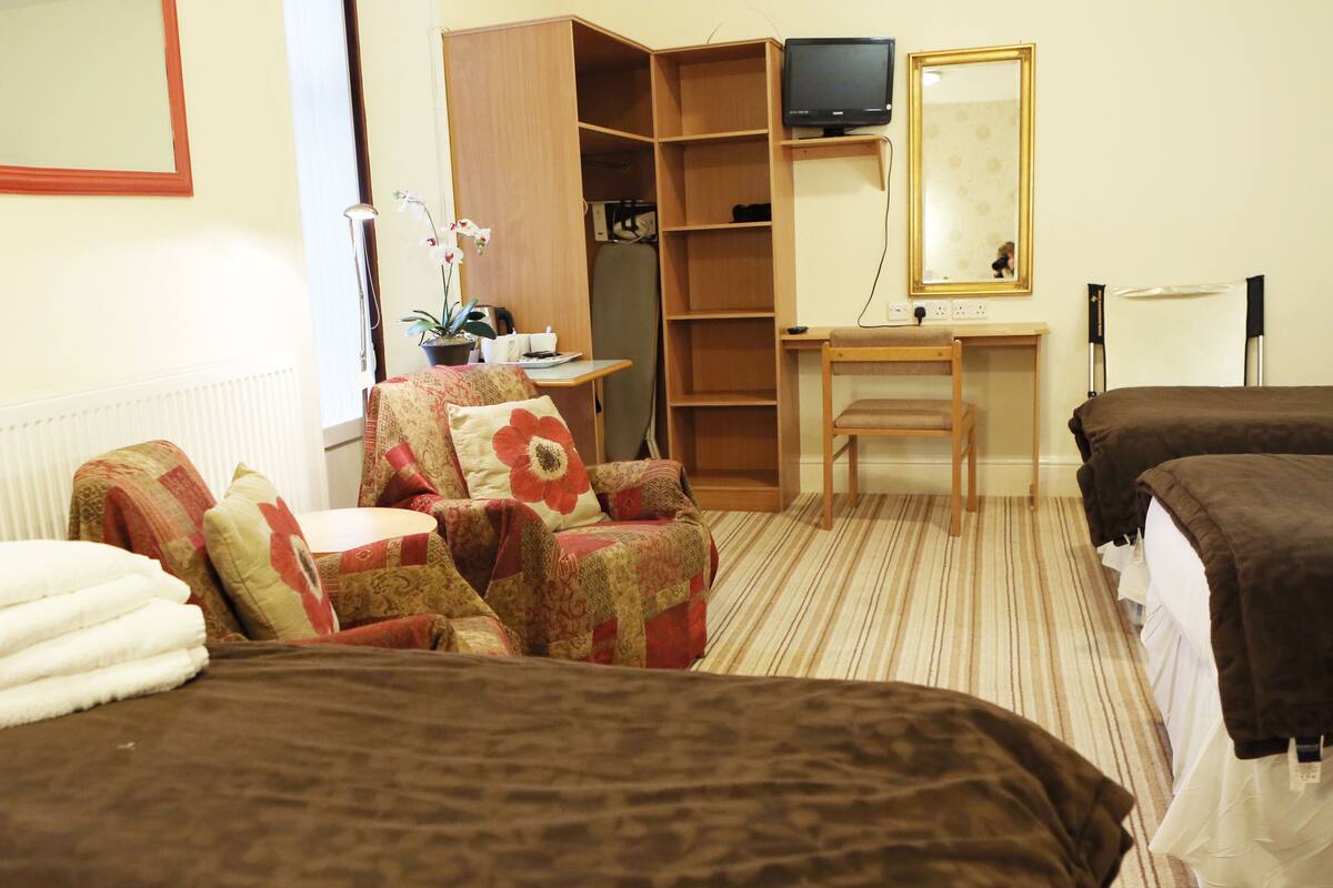 A hotel room with two beds, a desk, a chair, a television, and a wardrobe.